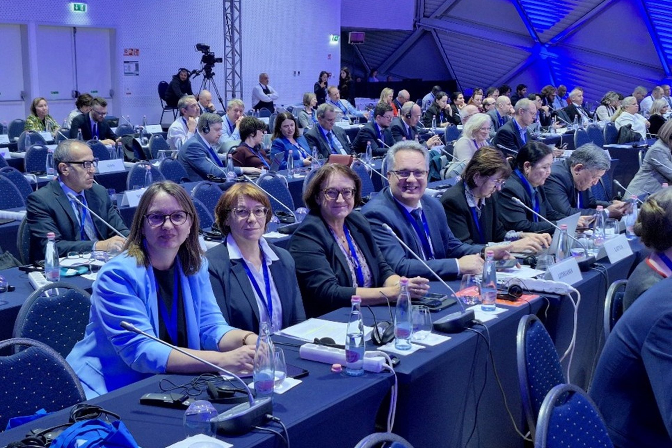 Žmonės sėdi prie stalų konferencijos salėje
