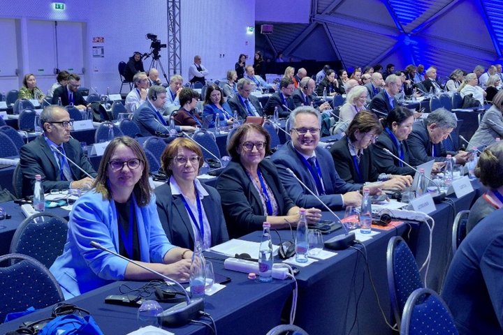 Žmonės sėdi prie stalų konferencijos salėje